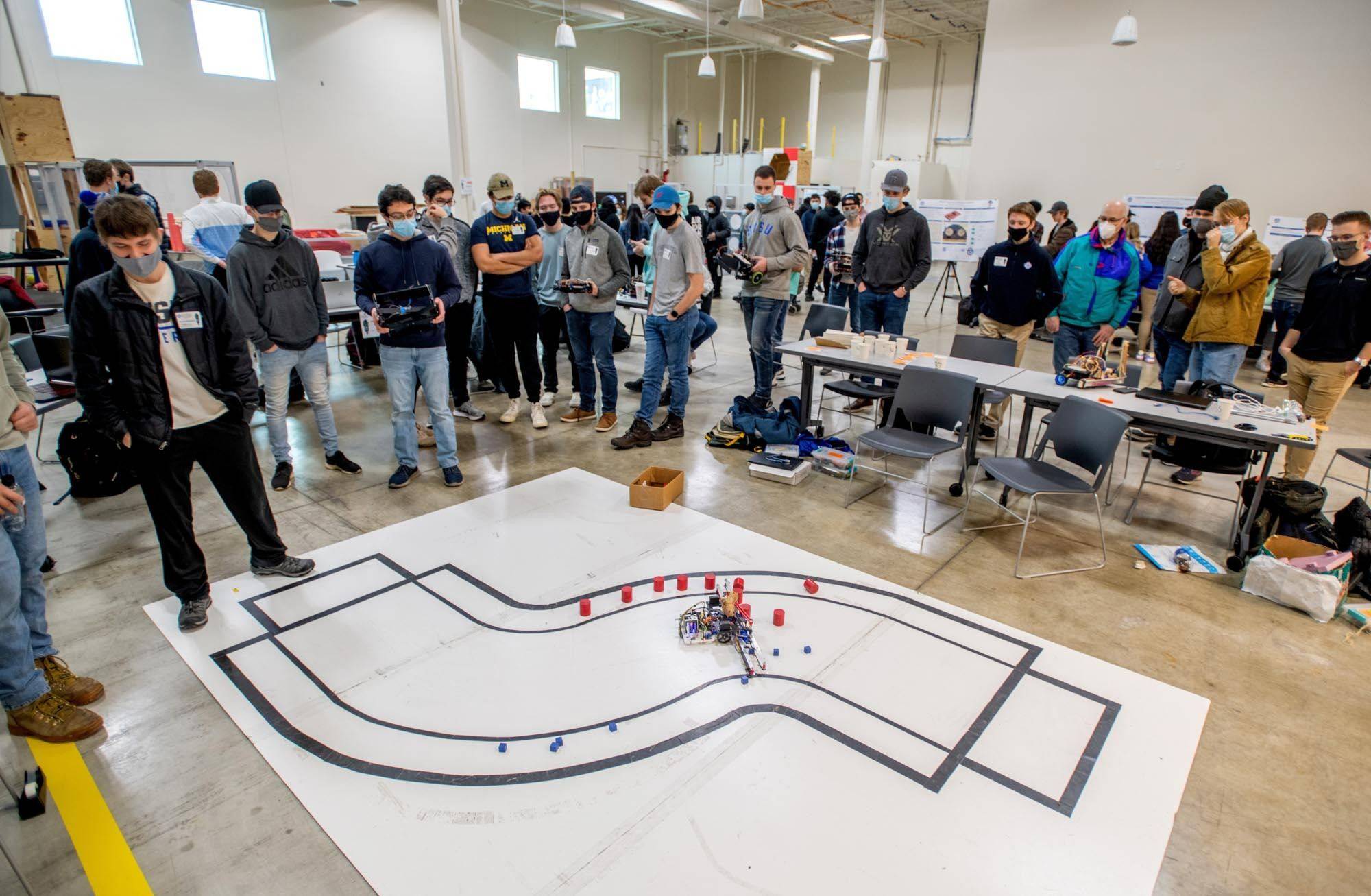 A crowd of visiting students watch a line-following robot on a robotics course at Project Day.